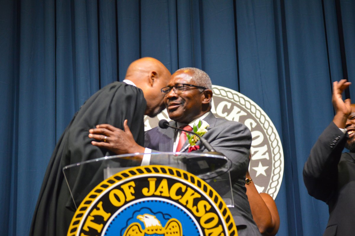 Mayor John Horhn wearing a grey suit and red tie hugs Judge graves wearing a black robe