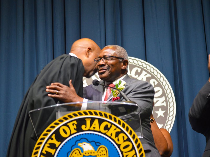 Mayor John Horhn wearing a grey suit and red tie hugs Judge graves wearing a black robe