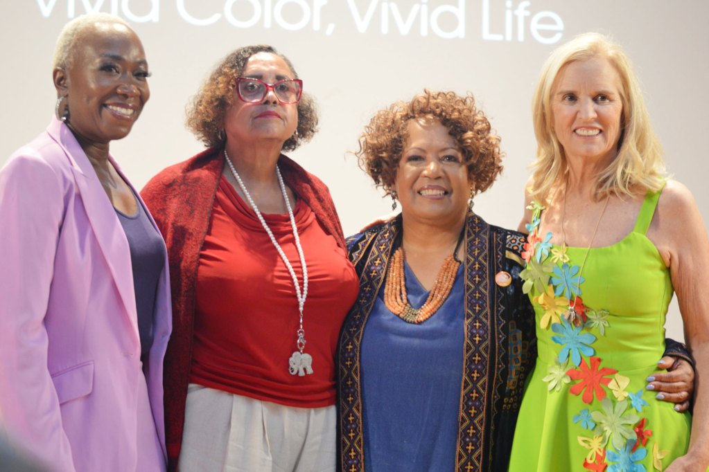 Women posed together for a photo wearing purple, red, blue, and green