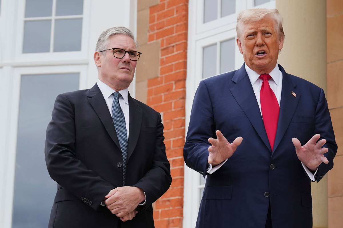 Keir Starmer stands on the left, listening, as Donald Trump speaks outside of a red brick building
