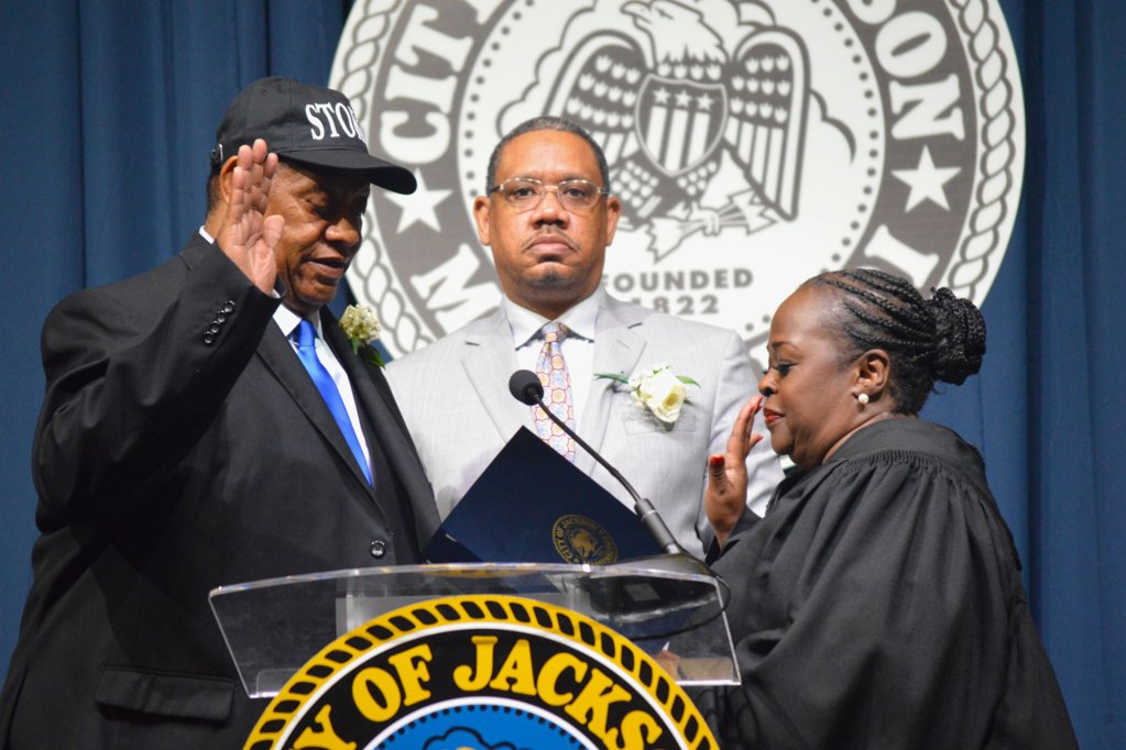 Councilman Kenneth Stokes wearing a black suit with a blue tie stands with his son while being sworn in by a judge wearing a black robe