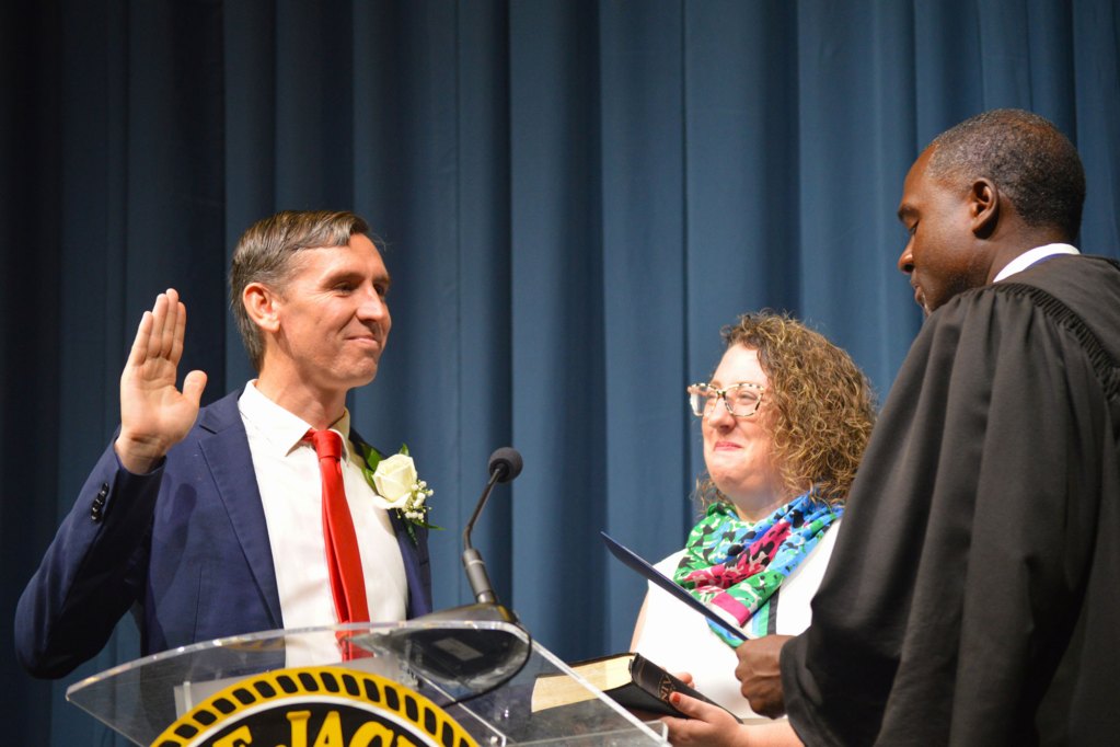 Kevin Parkinson wearing a blue suit and red tie stands with family while being sworn in by a judge wearing a black robe