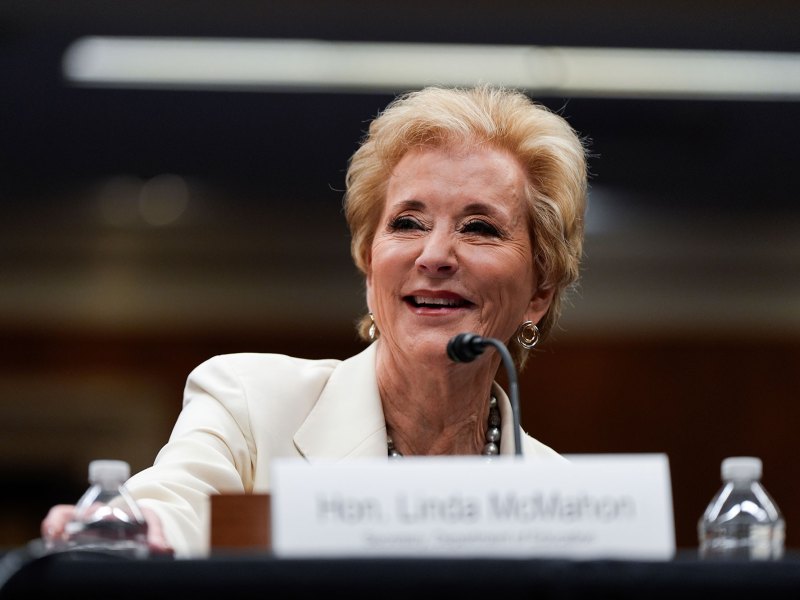 Linda McMahon in all white sits behind a table at a hearing.
