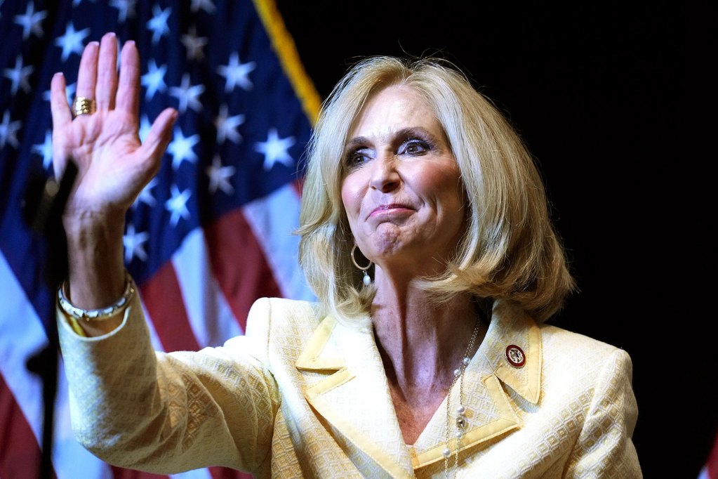 A woman in yellow waves on stage before a US Flag