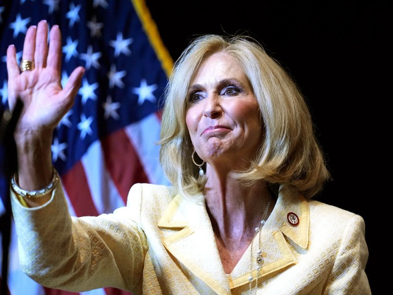 A woman in yellow waves on stage before a US Flag