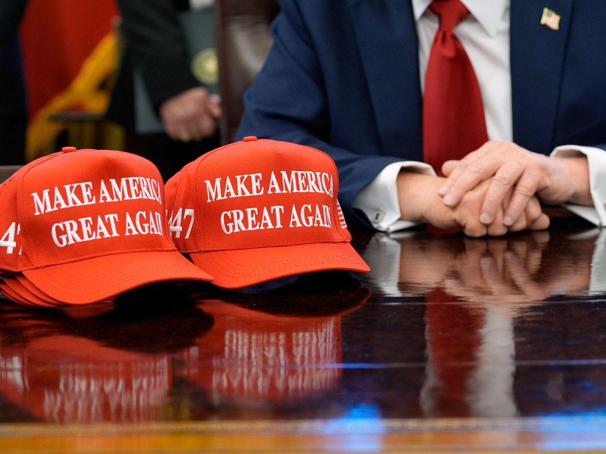 Red hats that read “Make America Great Again” sit beside President Donald Trump on his desk