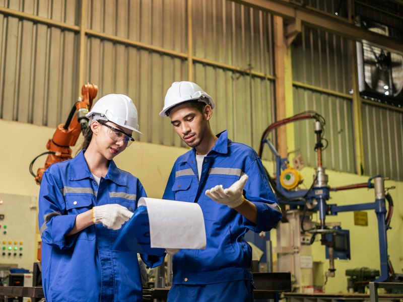 A man and a woman look over paperwork on a clipboard inside of a manufacturing warehouse