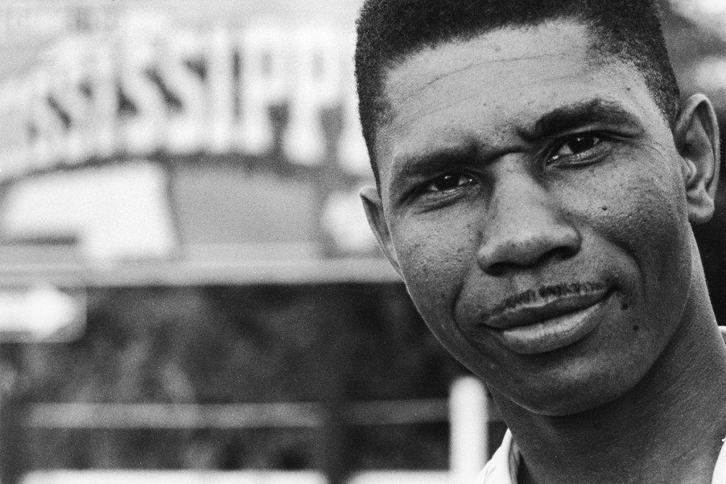 A closeup of Medgar Evers. A sign for Mississippi is seen behind him