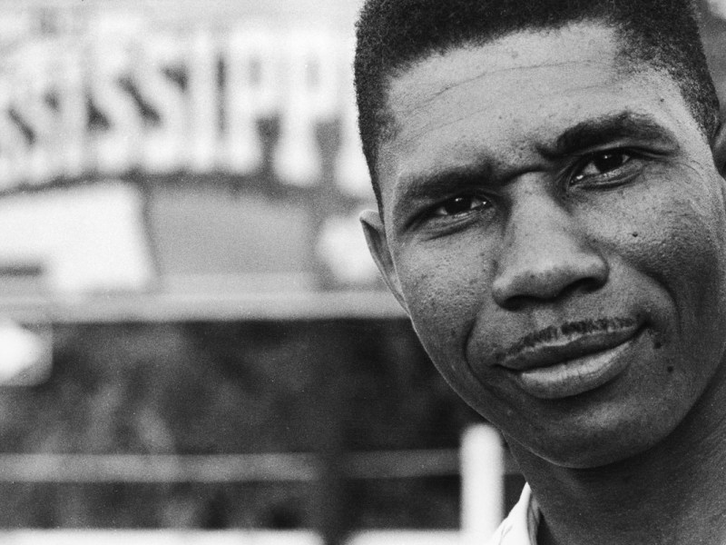 A closeup of Medgar Evers. A sign for Mississippi is seen behind him