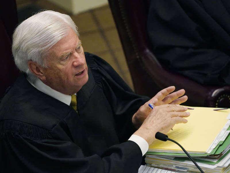 An above view of a judge speaking, a pile of files sitting before him