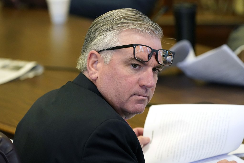 Photo of Mike Thompson, glasses askew as he looks behind him at someone