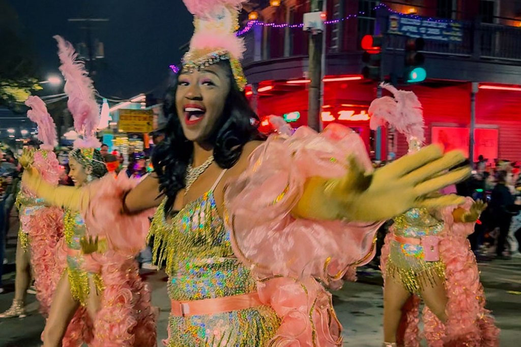 Women in glitzy pink and green costume prance down a street in a New Orleans Mardi Gras parade
