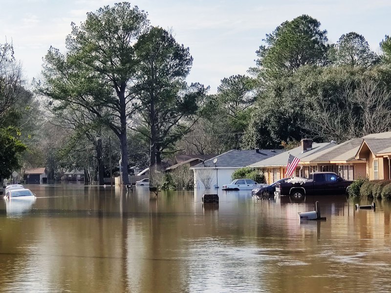A neighborhood street flooded, with water reaching up into cars and houses