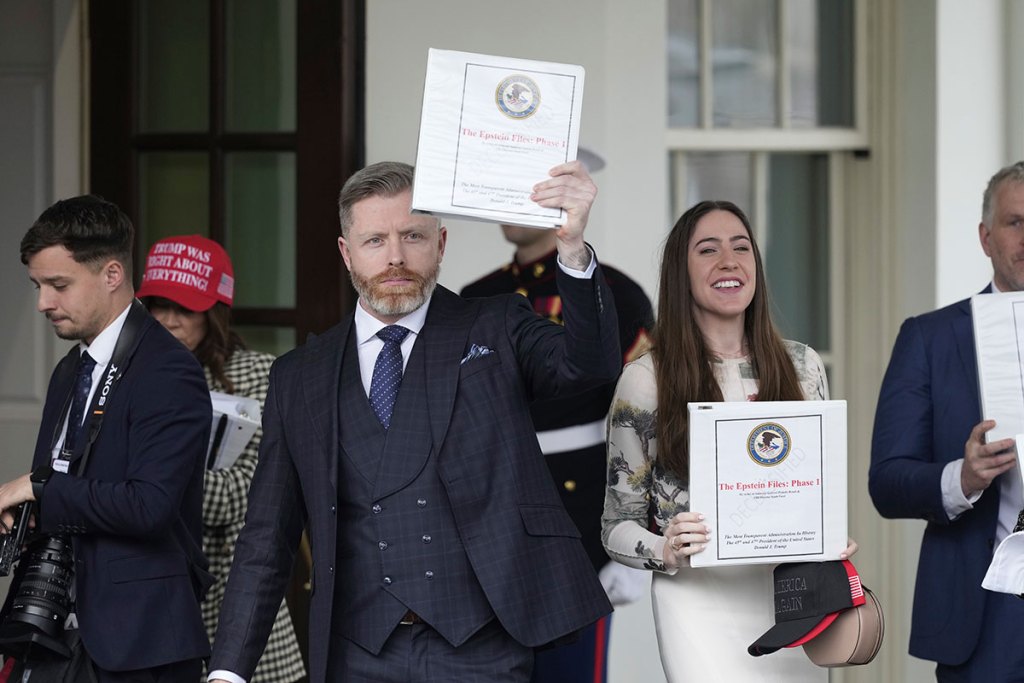 A man holds up a notebook labeled 'The Epstein Files: Phase 1' outside of the White House