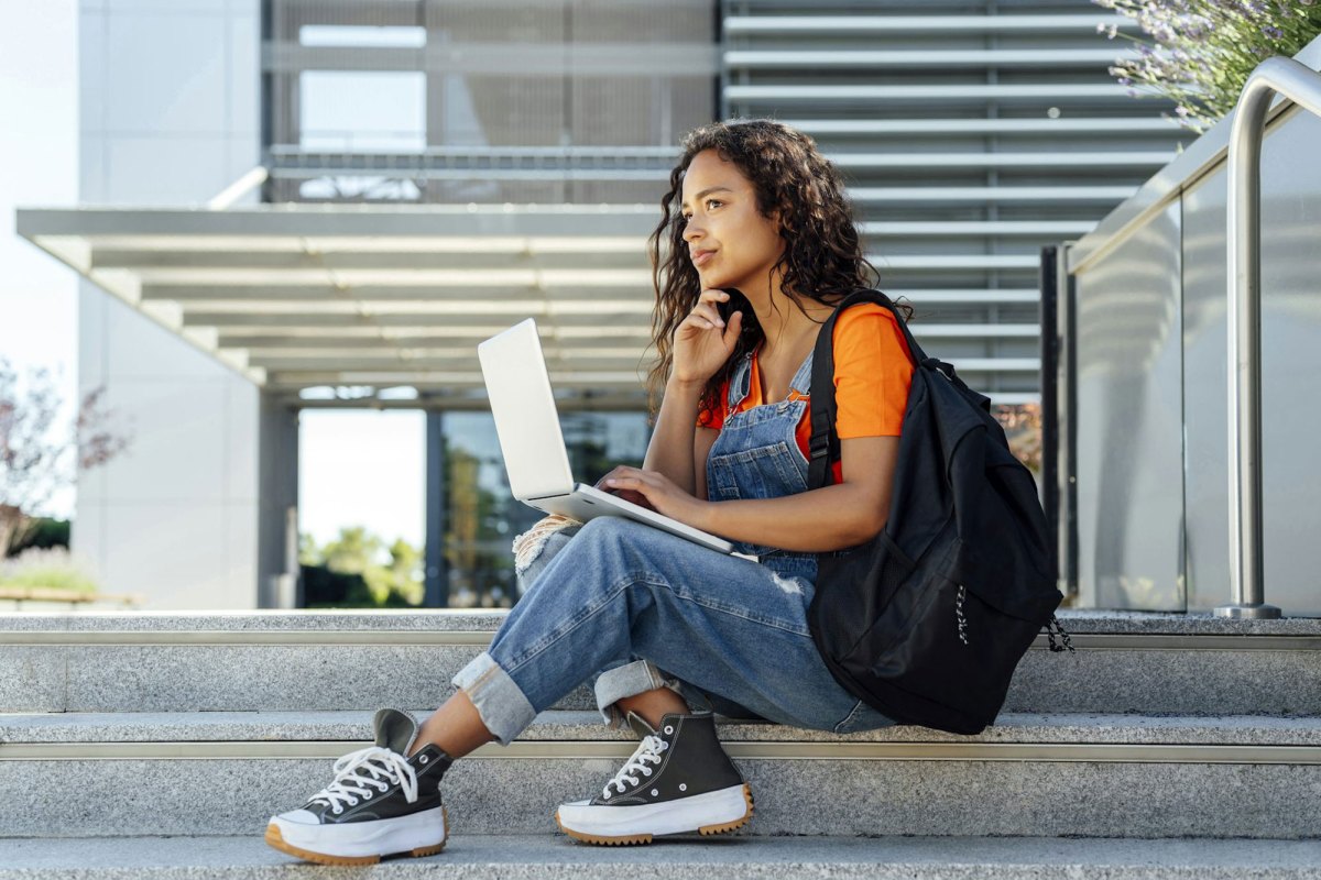 A student sitting on an exterior staircase by the school, laptop out
