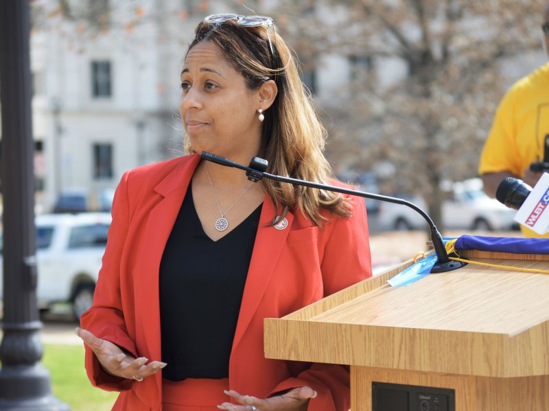 Zakiya Summers wearing a orange suit with a black shirt stands at a podium with a mic