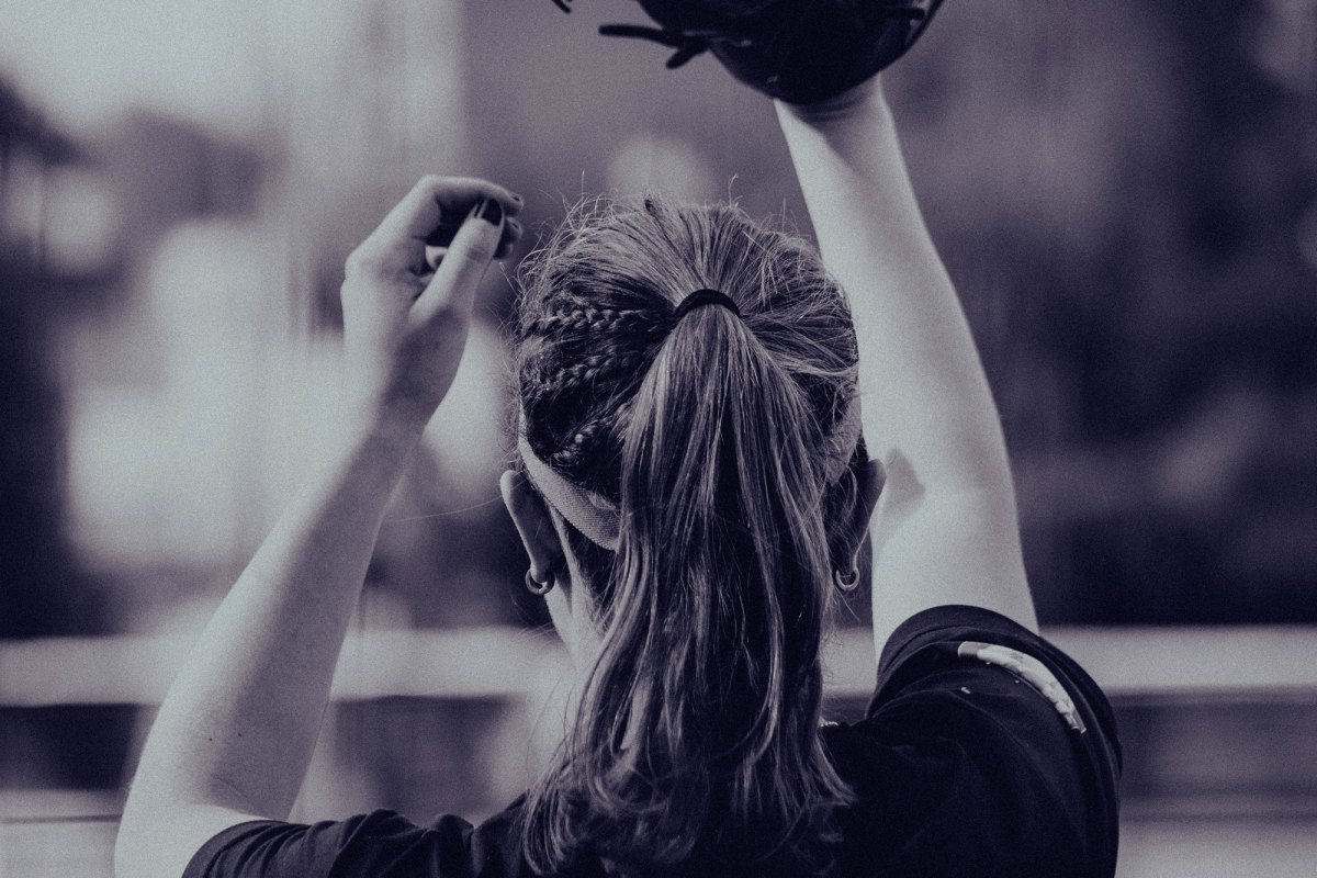 A view of the back of a woman playing baseball, gloved hand in air