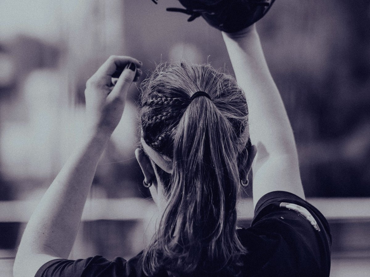 A view of the back of a woman playing baseball, gloved hand in air
