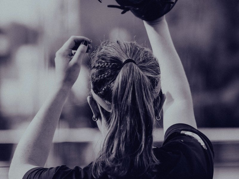 A view of the back of a woman playing baseball, gloved hand in air