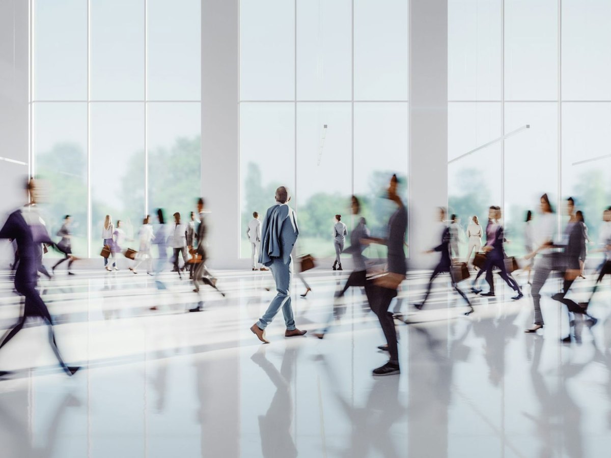 A large white interior room with people walking back and forth, blurred with motion