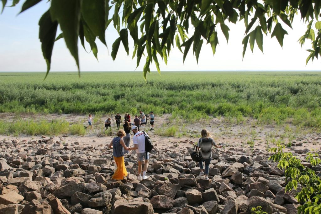 People walk through an area of rocks to a grassy plain