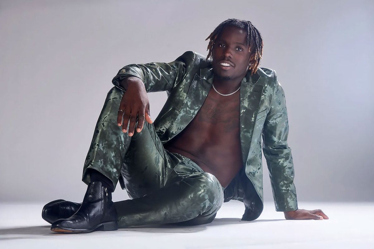 Singer Jamal Roberts sitting on the ground of a white backdrop wearing a green suit with no shirt