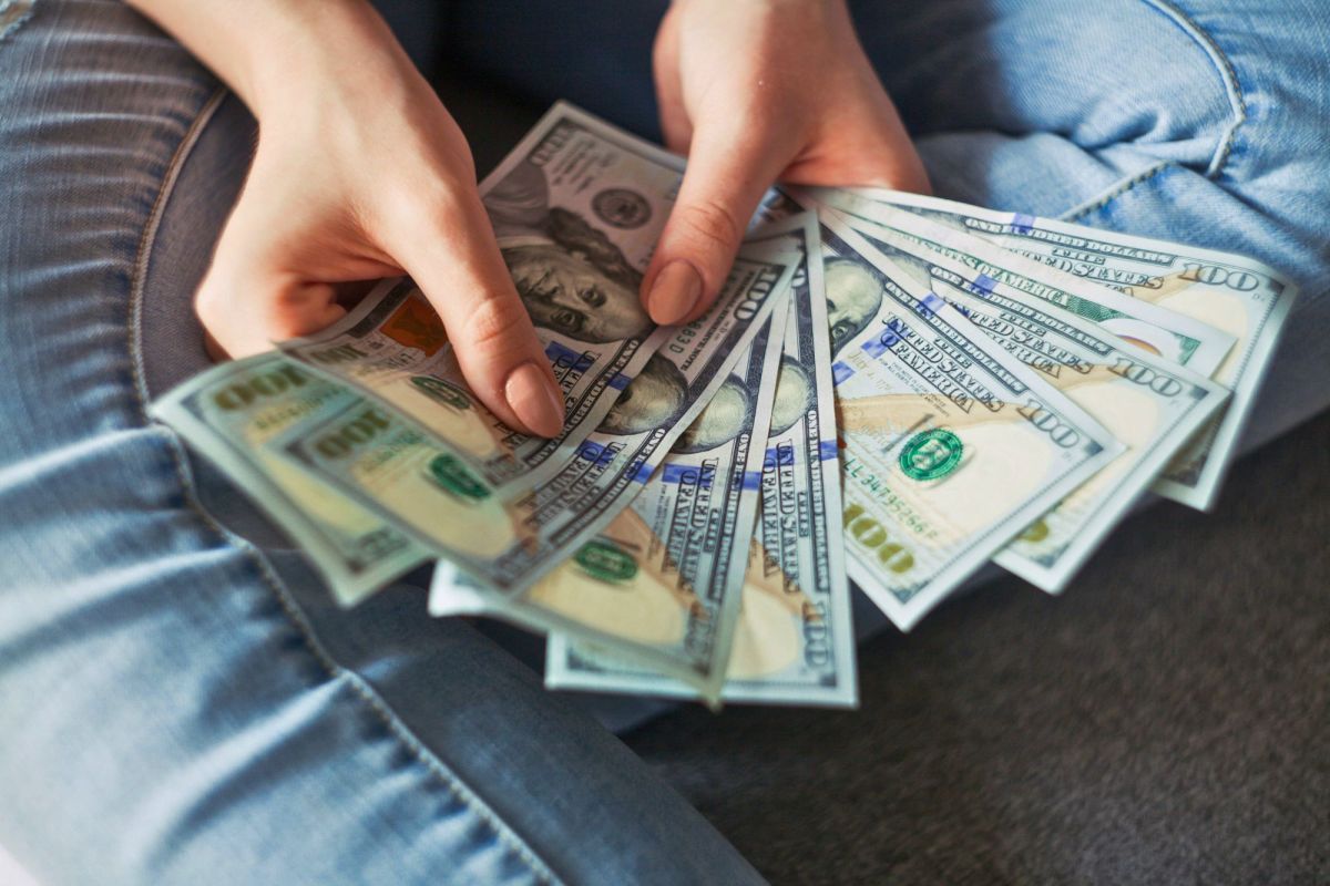 Two hands seen holding fanned out one hundred dollar bills