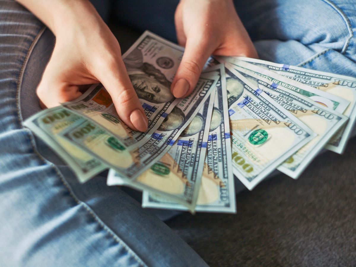 Two hands seen holding fanned out one hundred dollar bills