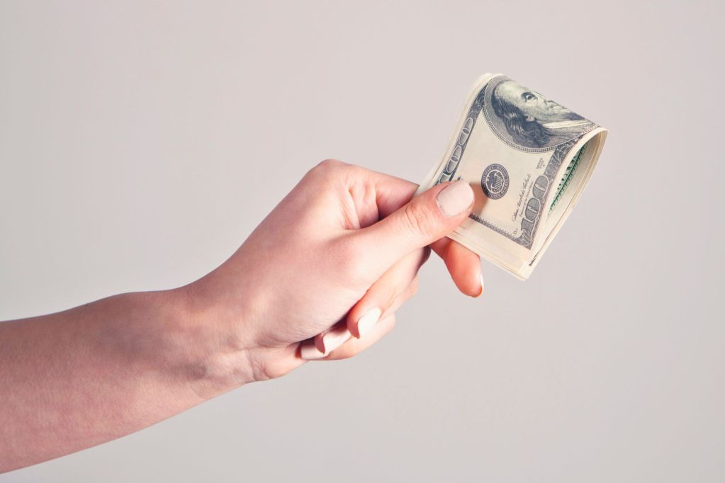 A hand holding folded hundred dollar bills