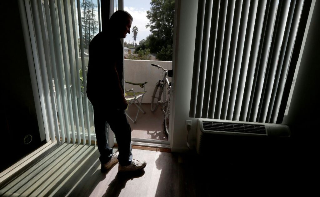 Silhouette of older man standing at sliding glass door.