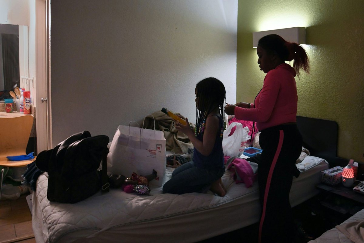 A woman does a girl's hair on a crowded hotel bed