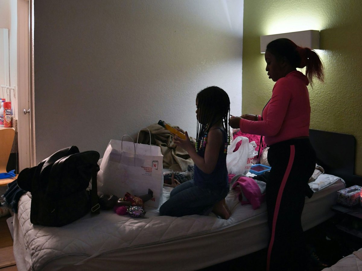 A woman does a girl's hair on a crowded hotel bed