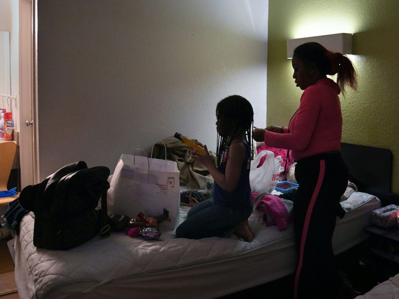 A woman does a girl's hair on a crowded hotel bed
