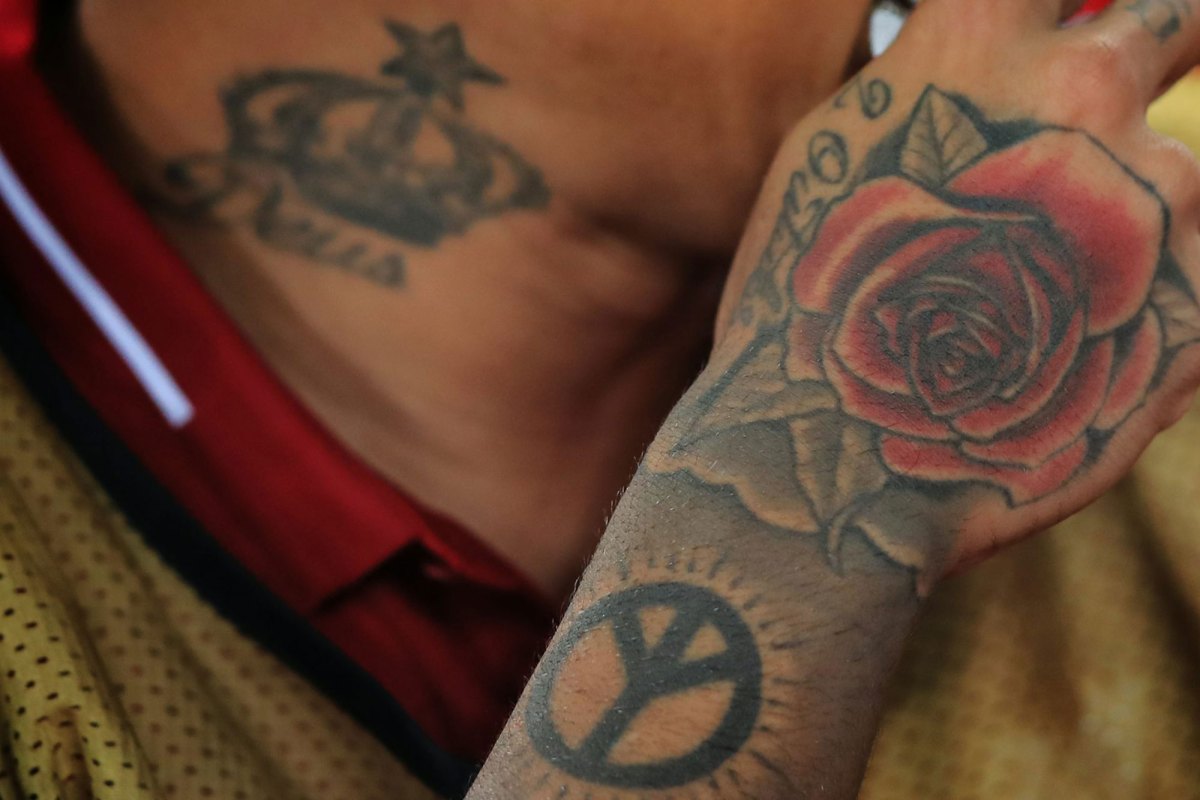 A closeup of tattoos on a person's hand and neck, designs including roses, crowns and a peace sign