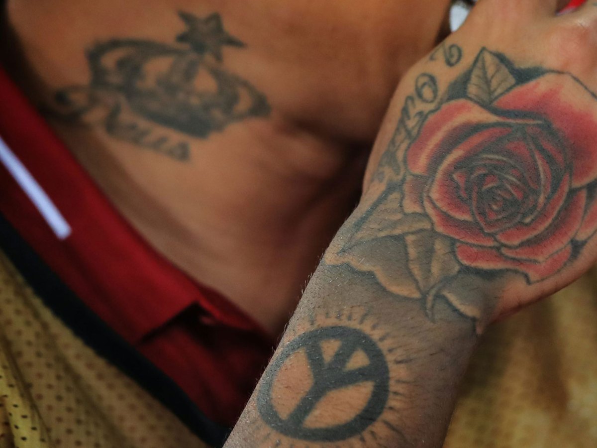 A closeup of tattoos on a person's hand and neck, designs including roses, crowns and a peace sign