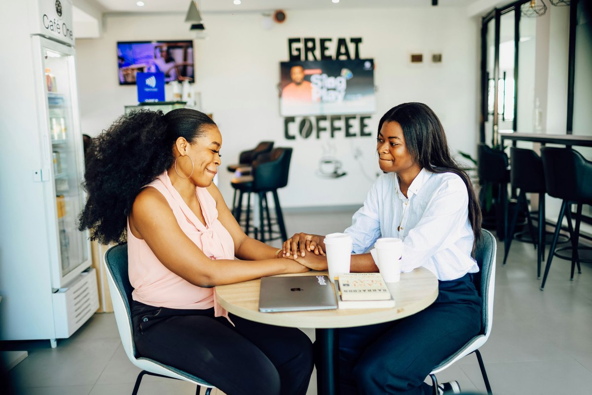Two friends meeting at a cafe holding each other's hands and smiling at each other