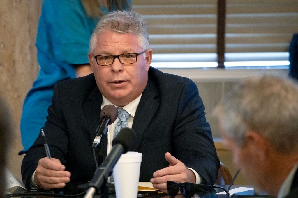 Rep. Rob Roberson talks into a microphone while sitting at the head of a large table.