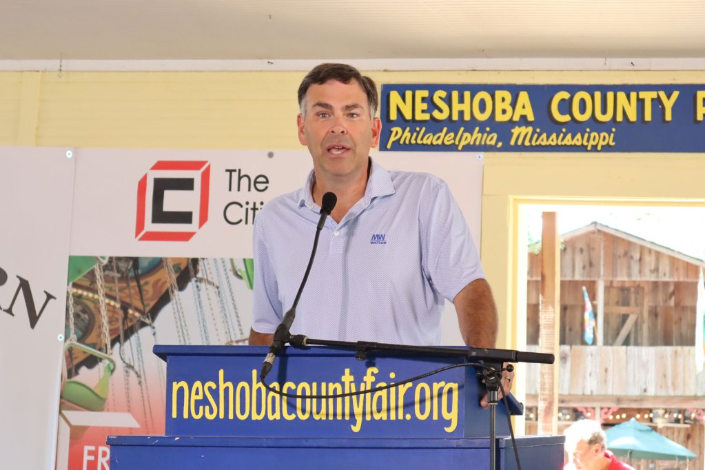 Michael Watson stands behind a podium and speaks into a microphone at the Neshoba County Fair