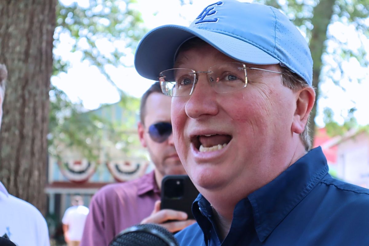 Tate Reeves, in blue baseball cap, speaks outside