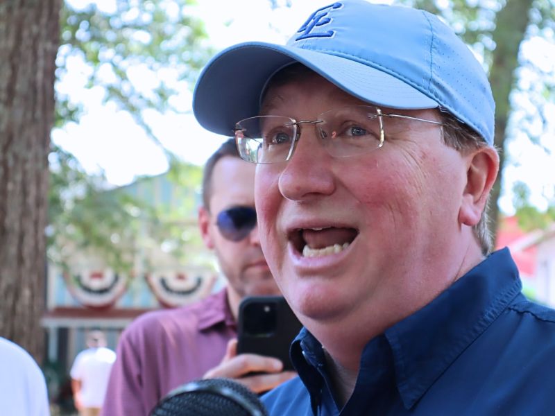 Tate Reeves, in blue baseball cap, speaks outside