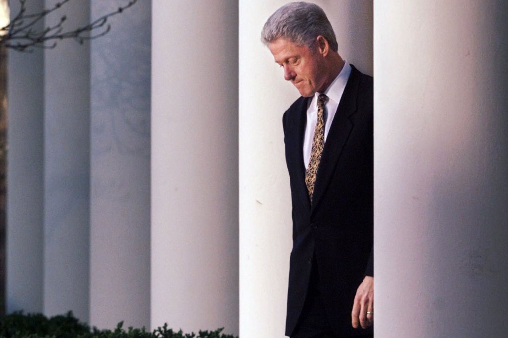 Bill Clinton stands between white columns, looking down