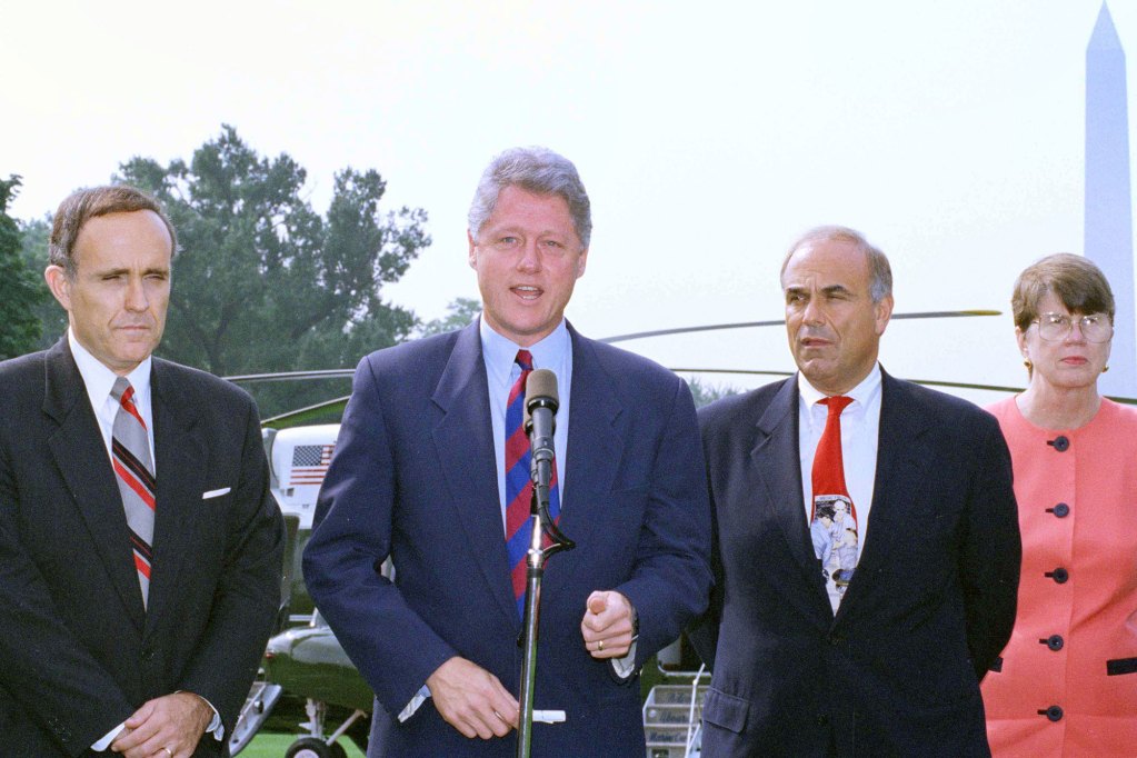 Bill Clinton speaks outside in front of a helicopter. Rudolph Giuliani and two others stand beside him