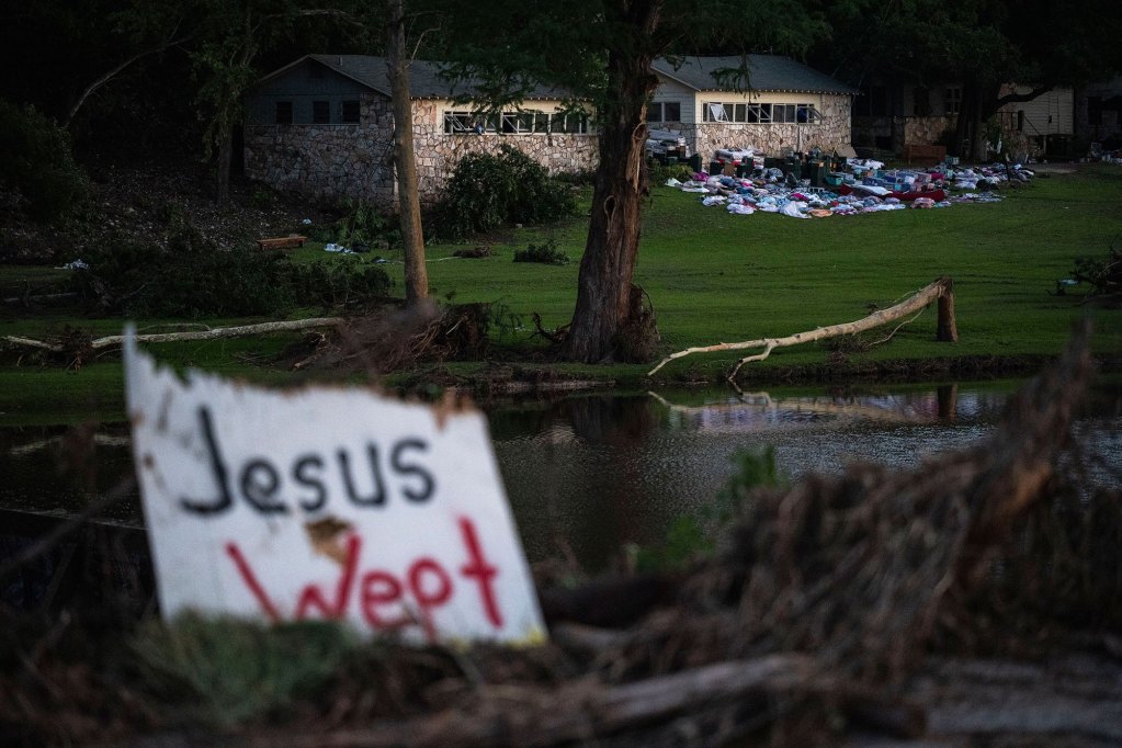 A sign reads Jesus Wept by a flowing river, and flooding damage visible