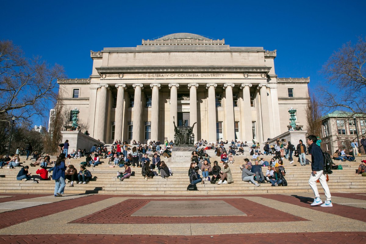 Students sit on the steps of a white columned building labeled The Library of Columbia University