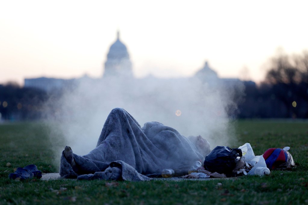 A man sleeping on the ground with a steam cloud behind him, and the silhouette of the Capitol building in the background