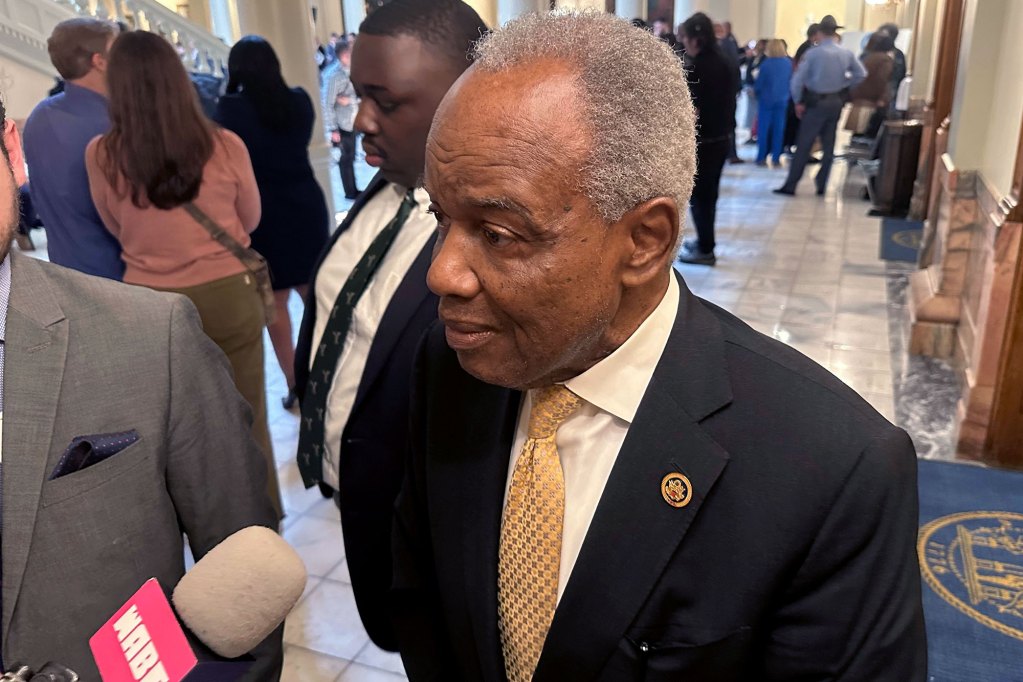 A man in a suit and gold tie speaks to a reporter inside a capitol building