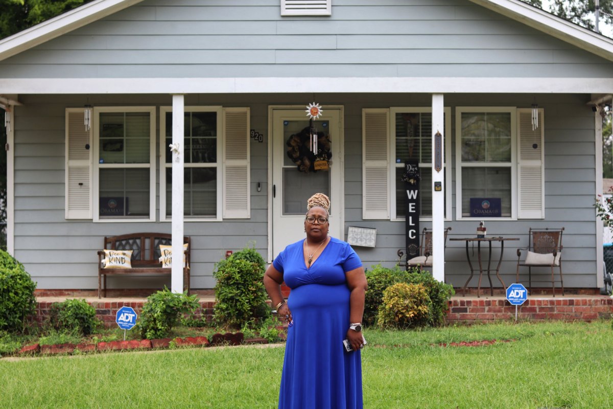 A woman in a blue dress stands outside of a light blue home