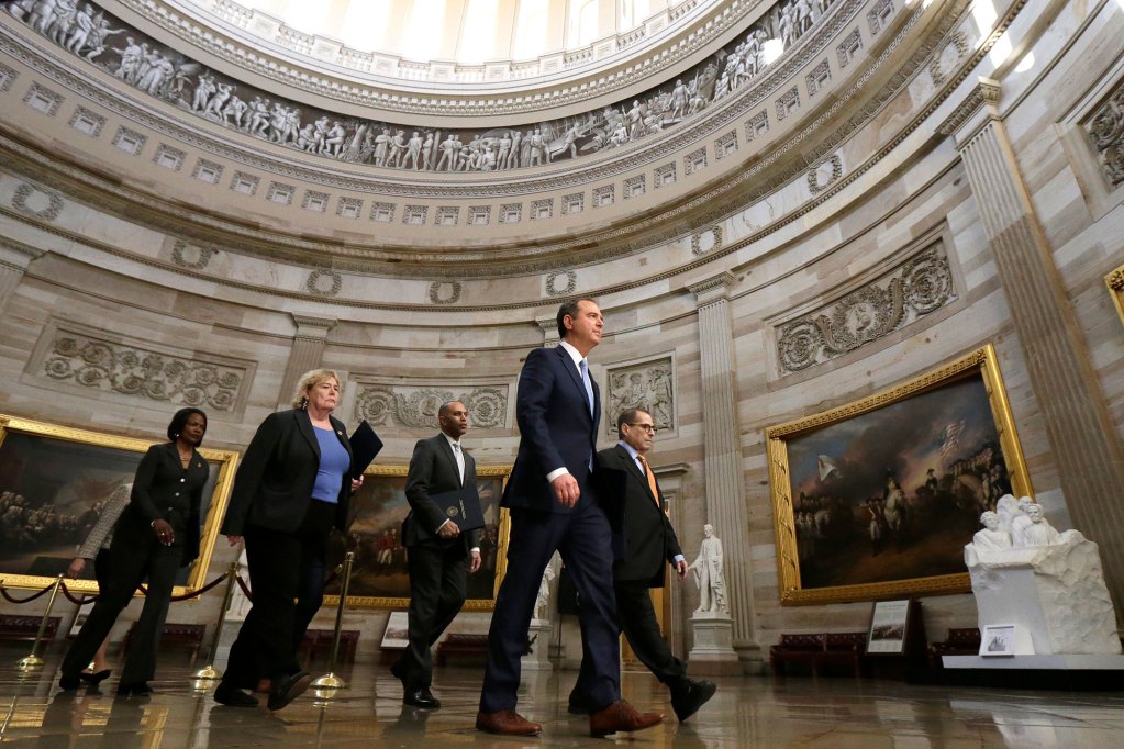 Five democratic party members walk across a marbel walled room