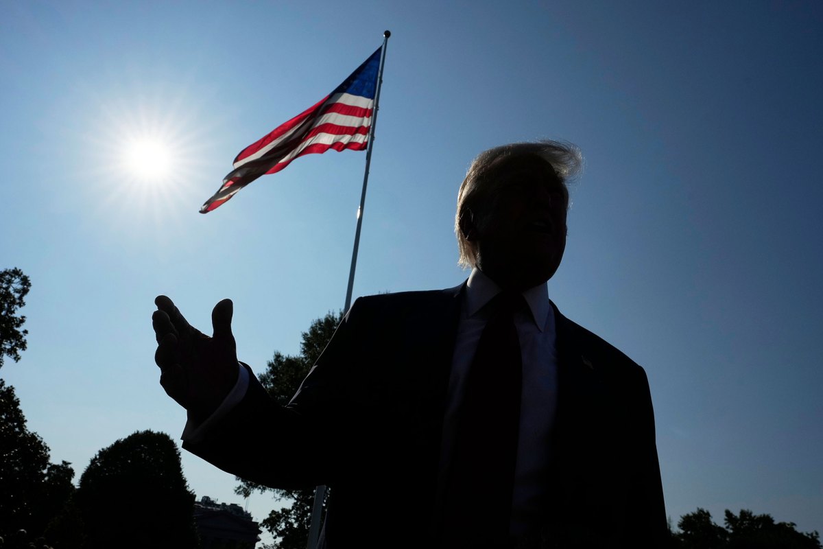 A dark silhouette of Donald Trump talking outside with the sun and a US Flag visible behind him