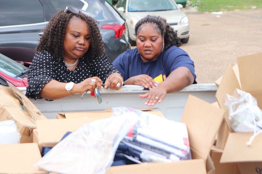 two women looking into the bed of a pickup truck filled with school supplies
